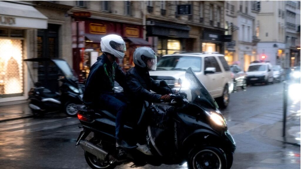 Motociclista com garupa usando capa de chuva.