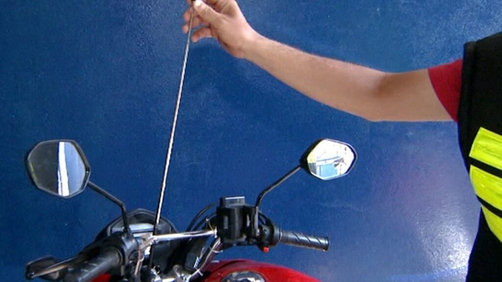 homem segurando antena corta pipa na moto.