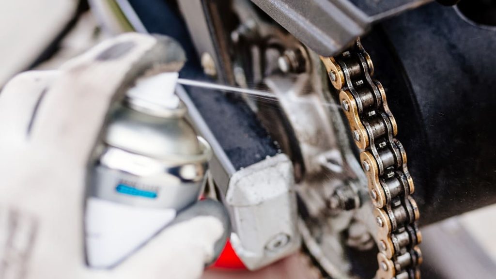 Mecânico aplicando lubrificante na corrente da moto.